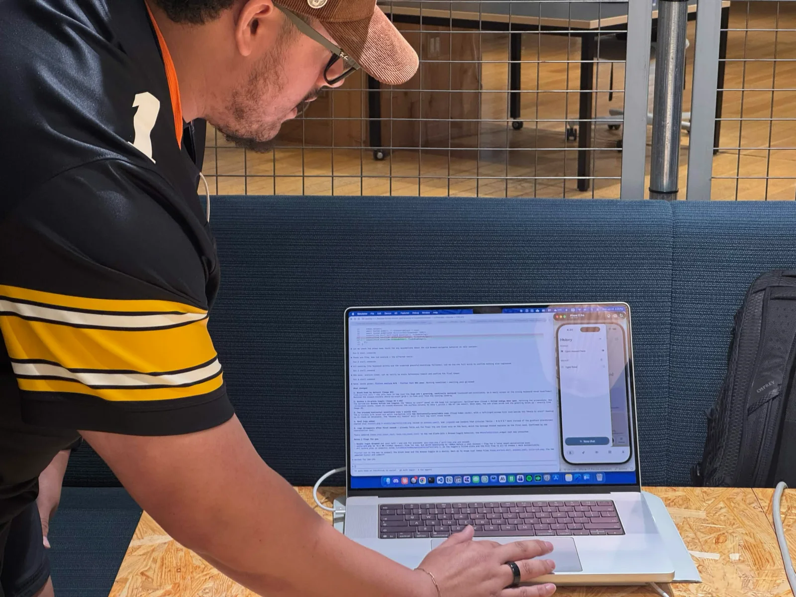 David leaning over a laptop at a work table, with a phone simulator open beside the code.